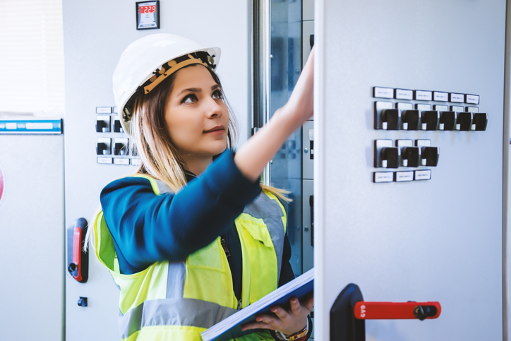 A facility maintenance engineer holding a tablet checks a control panel